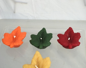 May include: Four leaf-shaped candles in orange, green, red, and yellow. The candles are in the shape of maple leaves.