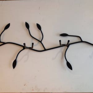 Könnte beinhalten: Schwarzer Wand-Kleiderhaken aus Metall in Form eines Astes mit Blättern. Der Haken hat mehrere Haken zum Aufhängen von Gegenständen.