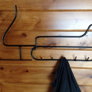May include: Black metal coat rack shaped like a snowmobile with five hooks. A black jacket is hanging on one of the hooks.