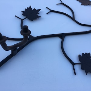 Könnte beinhalten: Schwarze Wanddekoration aus Metall in Form eines Astes mit Blättern. Der Ast hat drei Haken zum Aufhängen von Gegenständen.