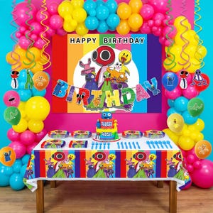 May include: A party table setup featuring a Rainbow Friends theme with a colorful backdrop, a tiered cake, plates, and blue plastic cutlery. The scene is decorated with a balloon arch in shades of pink, yellow, and blue, and a banner reading HAPPY BIRTHDAY.