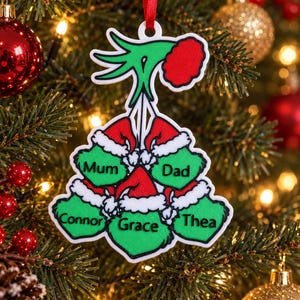 May include: A white-bordered Christmas ornament featuring a green hand holding five green stockings with red Santa hats. The stockings are labelled with the names Mum, Dad, Connor, Grace, and Thea in black text. It hangs from a red ribbon.