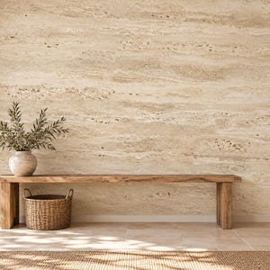 May include: A long wooden bench sits against a wall with beige travertine stone cladding. A ceramic vase containing olive branches rests on the bench, next to a woven wicker basket placed underneath on the floor.