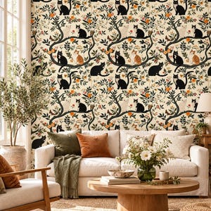 May include: Wallpaper featuring a repeating pattern of black, white, and orange cats perched on dark tree branches with orange flowers, green leaves, and small birds against a cream background. The design covers the wall behind a sofa.
