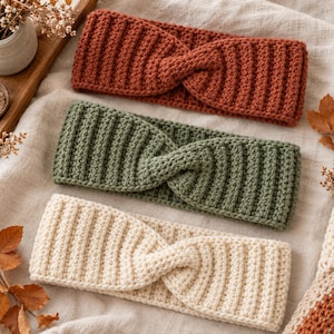 May include: Three knitted headbands featuring a ribbed texture and a central twist detail. The headbands are colored in rust orange, sage green, and cream. Each piece is constructed with a consistent vertical stitch pattern across the entire surface.