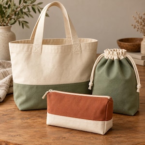 Peut inclure: Un ensemble de trois sacs en toile comprenant un grand cabas à panneaux crème et vert olive, une pochette à cordon en vert olive uni avec bordure crème, et une trousse rectangulaire à fermeture éclair avec haut rouille et base crème.