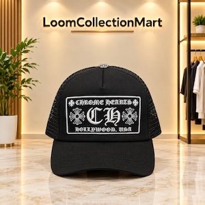 Könnte beinhalten: Eine schwarze Trucker-Cap mit einem rechteckigen weißen Aufnäher auf der Vorderseite. Der Aufnäher zeigt den Schriftzug CHROME HEARTS, die Buchstaben CH, den Text HOLLYWOOD, USA sowie Kreuzsymbole. Die Cap hat ein Netzgewebe an der Rückseite.