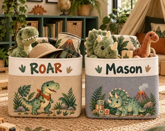 May include: Two rectangular fabric storage bins featuring dinosaur themes. The left bin is tan with the text ROAR and a green dinosaur. The right bin is gray with the text Mason and a triceratops dinosaur. Both bins contain plush dinosaur toys.