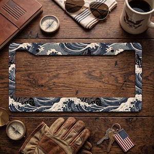 May include: A rectangular license plate frame featuring a repeating graphic pattern of dark blue and cream-colored stylized ocean waves with foam crests. The frame has two mounting holes at the top and a smooth, flat surface design.