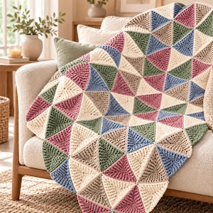 Puede incluir: Una manta de ganchillo con un patrón geométrico de triángulos en color crema, rosa empolvado, verde salvia y azul pizarra. El tejido está formado por motivos triangulares individuales unidos para crear una manta grande, texturizada y multicolor.