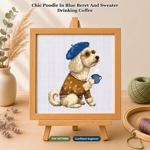 Op de afbeelding: Een kruissteekpatroon met een lichtgekleurde poedel die een blauwe baret, een ronde bril en een bruine trui met patroon draagt terwijl deze een blauwe koffiemok vasthoudt. De tekst luidt Chic Poodle In Blue Beret And Sweater Drinking Coffee.
