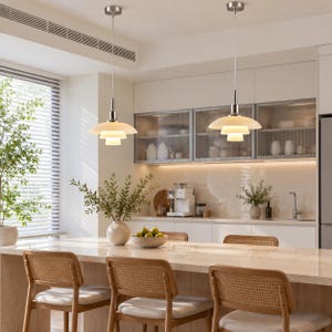 Op de afbeelding: Twee moderne hanglampen met gelaagde, witte glazen kappen en geborsteld nikkelen armaturen die aan het plafond hangen. Elk armatuur heeft een ontwerp met meerdere lagen dat het licht naar beneden verspreidt boven het keukeneiland.