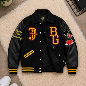 May include: A black varsity jacket with leather sleeves, featuring yellow and red embroidered patches including the letters J and BG, the text Better Than Yesterday, a heart with wings, and a mouse-ear icon. It has a quilted lining and snap buttons.