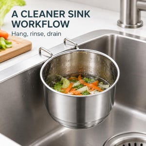 May include: A stainless steel sink colander with two hooks hanging from the edge of a kitchen sink. The container holds water and chopped vegetables. Text above reads: A CLEANER SINK WORKFLOW. Hang, rinse, drain.