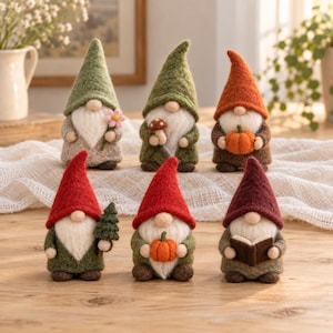 Peut inclure: Six figurines de gnomes en feutrine disposées sur deux rangées. La rangée supérieure présente des gnomes aux chapeaux verts, olive et orange tenant une fleur, un champignon et une citrouille. La rangée inférieure montre des gnomes aux chapeaux rouges et bordeaux tenant un arbre, une citrouille et un livre.