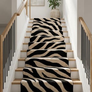 May include: A staircase featuring a runner with a black and cream zebra stripe pattern. The stairs have light wood treads and white risers, flanked by wooden handrails with black metal balusters. A potted green plant sits on the landing above.