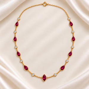 May include: A gold chain necklace featuring alternating teardrop-shaped red gemstones and small round clear stones. The necklace is arranged in a symmetrical pattern with a single marquise-cut red gemstone centered at the bottom of the chain.