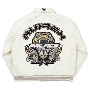 Könnte beinhalten: Eine cremeweiße Jacke mit einer großen Grafik auf der Rückseite, die eine Schlange mit Fangzähnen, den Schriftzug AVIREX und PALACE sowie die Zahlen 2020 zeigt. Das Design enthält schwarze, beige und weiße Akzente mit Karomustern und Flammen.