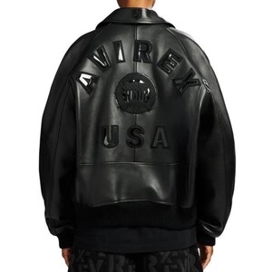 May include: A black leather bomber jacket featuring a large, embossed AVIREX USA logo on the back. The design includes a circular emblem in the center, long sleeves with ribbed cuffs, and a ribbed hem. The jacket has a structured collar and a smooth finish.