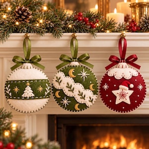 May include: Three round felt Christmas ornaments hanging from a mantel. The left is white with a green band and embroidered tree. The center is green with white clouds, moons, and stars. The right is red with a white star and Santa hat.