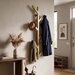 May include: A wall-mounted coat rack shaped like a tree branch with a metallic gold finish. The rack features multiple angled hooks holding a tan fedora, a navy blue trench coat, a green scarf, and a set of silver keys hanging from a hook.