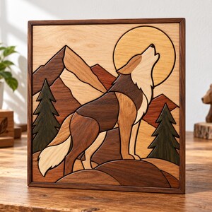 May include: A square wooden wall art piece featuring an intricate marquetry design of a wolf howling at a large circular moon. The scene includes layered mountain peaks, two dark green pine trees, and a wolf composed of various wood tones.