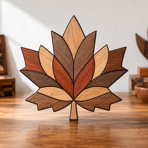 May include: A decorative maple leaf sculpture crafted from multiple segments of wood in varying natural tones, including light tan, medium brown, dark chocolate, and reddish-brown, featuring dark outlines between each individual wooden piece.