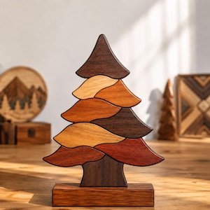 May include: A decorative wooden tree sculpture composed of interlocking, curved segments in varying shades of brown, ranging from light tan to dark espresso. The tree stands on a rectangular wooden base, featuring a smooth, polished finish.