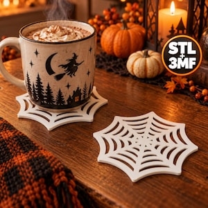 May include: A ceramic mug filled with a hot beverage topped with whipped cream, featuring a black silhouette of a witch on a broomstick, a crescent moon, and a forest scene. Two white spiderweb-shaped coasters sit on a wooden surface.