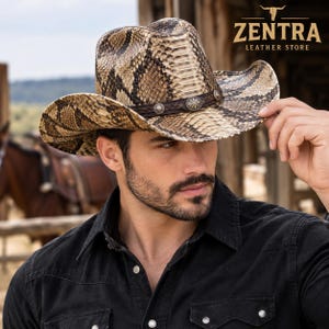 May include: A cowboy hat featuring a brown and tan snakeskin pattern with a dark brown braided leather hat band adorned with silver-toned metal concho accents. The text ZENTRA LEATHER STORE is visible in the upper right corner of the image.