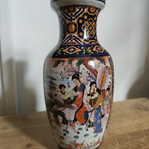 May include: A ceramic vase featuring a narrow neck and a bulbous body decorated with a detailed scene of figures in traditional attire, including a person on horseback, surrounded by floral motifs and geometric patterns in blue, gold, and orange.