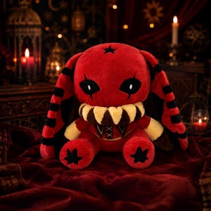 May include: A plush toy featuring a red rabbit-like creature with long ears marked by black stripes. It has a large, cream-coloured toothy collar, black star-shaped markings on its forehead and feet, and sharp, almond-shaped black eyes.
