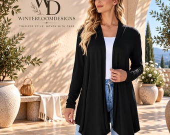 Puede incluir: Un cárdigan negro de manga larga abierto por delante con dobladillo drapeado, usado sobre una camiseta blanca y jeans azul claro desgastados. La imagen incluye el texto WD WINTERLOOMDESIGNS TIMELESS STYLE, WOVEN WITH CARE en la esquina.