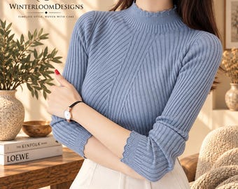 Puede incluir: Un suéter de manga larga en color azul claro con textura de punto acanalado, cuello alto y bordes festoneados en los puños. La prenda muestra el logotipo de WinterloomDesigns en la esquina superior izquierda con el texto Timeless Style, Woven With Care.