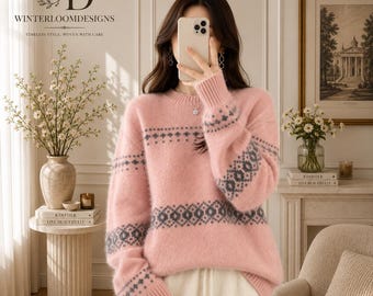 Puede incluir: Un suéter de manga larga de color rosa claro, suave y difuso, con cuello redondo y un patrón geométrico gris oscuro repetido en el pecho y las mangas. El suéter tiene puños y dobladillo acanalados, lo que proporciona un ajuste relajado.