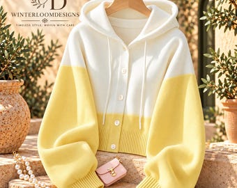 Puede incluir: Un cárdigan con capucha bicolor que presenta una sección superior blanca y una sección inferior de color amarillo suave con mangas amarillas a juego. La prenda incluye cierre frontal de botones, capucha con cordones y puños acanalados.