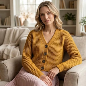 Peut inclure: Un cardigan en tricot côtelé jaune moutarde avec un col en V et quatre boutons marron foncé sur le devant. Ce vêtement à manches longues est porté sur une jupe plissée rose clair, créant un ensemble superposé à la texture côtelée.