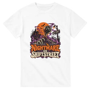 Op de afbeelding: Een wit t-shirt met een grafische print van een skeletachtige hand die uit een weg omhoog komt om een handmatige versnellingspook vast te pakken. Het ontwerp bevat een spookhuis, vleermuizen, een straatnaambord met SHIFT STREET en de tekst NIGHTMARE ON SHIFT STREET.