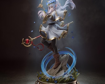 Puede incluir: Una figura de fantasía de un personaje elfo con largo cabello blanco, vistiendo un vestido blanco con bordes dorados y una corona de flores azules. El personaje sostiene un bastón rojo con una esfera roja sobre una base rocosa.