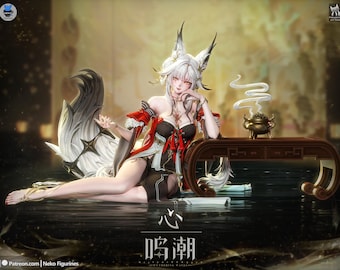 Puede incluir: Una figura de estilo anime con cabello blanco, orejas de zorro y una gran cola fluida. El personaje viste un atuendo negro y rojo con detalles dorados, recostado junto a un pequeño quemador de incienso sobre una mesa oscura.