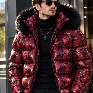 Könnte beinhalten: Eine rote und schwarze Daunenjacke mit Schlangenledermuster und einer Kapuze mit schwarzem Kunstfellbesatz, getragen über einem schwarzen Rollkragenpullover. Die Jacke hat eine glänzende Oberfläche, einen Frontreißverschluss und lange Ärmel.