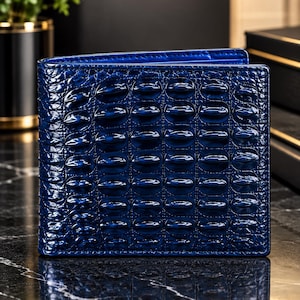 Puede incluir: Una cartera plegable con un acabado azul profundo y brillante, con un patrón texturizado en relieve que imita la apariencia de la piel de cocodrilo. La superficie tiene un brillo pulido y reflectante, con bordes limpios y rectos.