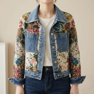 Pode incluir: Um casaco de ganga com um padrão floral de tapeçaria nas mangas e painéis frontais, com bolsos, gola e punhos em ganga azul sólida. O casaco tem um fecho frontal com botões de metal prateado e mangas compridas.