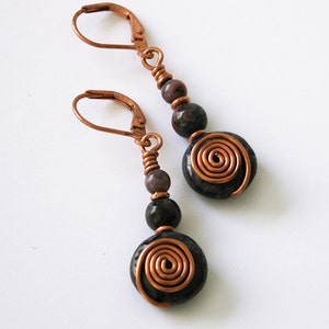 May include: A pair of copper wire wrapped earrings with dark brown and light brown agate beads. The earrings have a spiral design.