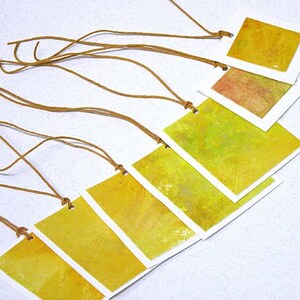 May include: Six yellow watercolor gift tags with brown twine attached. The tags are rectangular and have a white border. The watercolor is a light yellow with some darker yellow accents.
