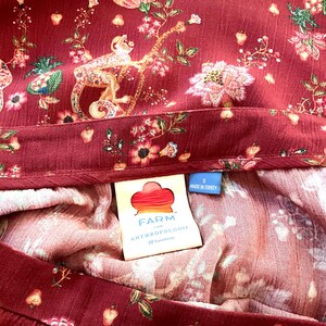 Pode incluir: Uma saia de estampa floral vermelha e branca com uma cintura marrom. A saia tem uma etiqueta que diz "FARM for ANTHROPOLOGIE" e "Feito na Turquia".