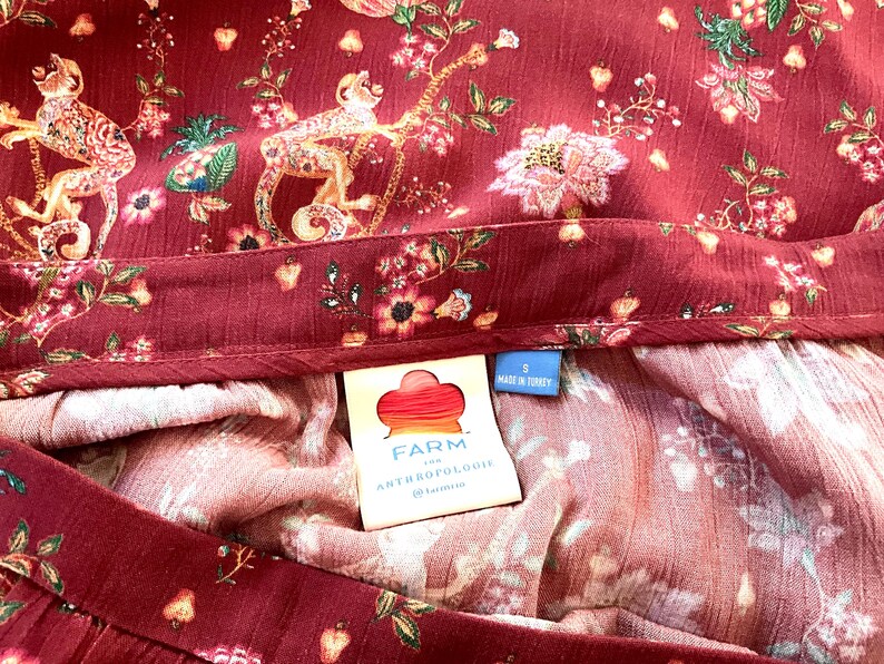 Pode incluir: Uma saia de estampa floral vermelha e branca com uma cintura marrom. A saia tem uma etiqueta que diz "FARM for ANTHROPOLOGIE" e "Feito na Turquia".