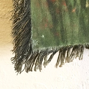May include: Close-up of the fringe on a green tapestry with a woven pattern. The fringe is a dark brown colour and is made of multiple strands of yarn.