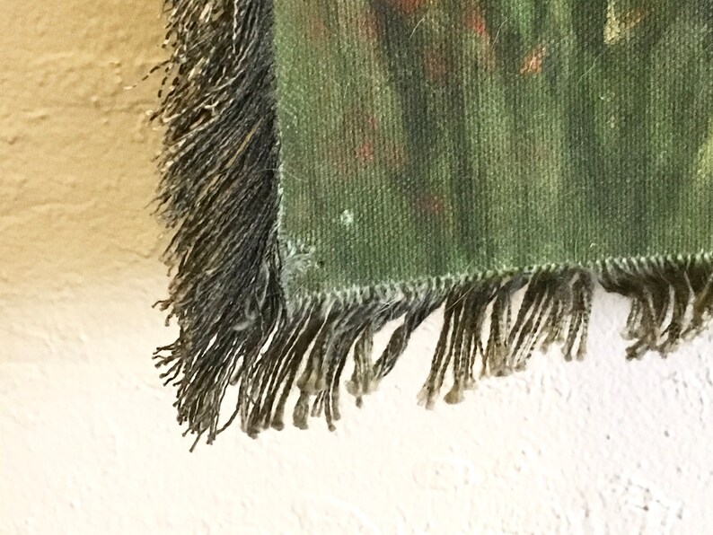May include: Close-up of the fringe on a green tapestry with a woven pattern. The fringe is a dark brown colour and is made of multiple strands of yarn.
