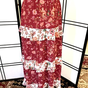 Pode incluir: Uma saia maxi longa, de cor bord&ocirc;, com estampa floral e v&aacute;rias camadas de acabamento branco com babados.
